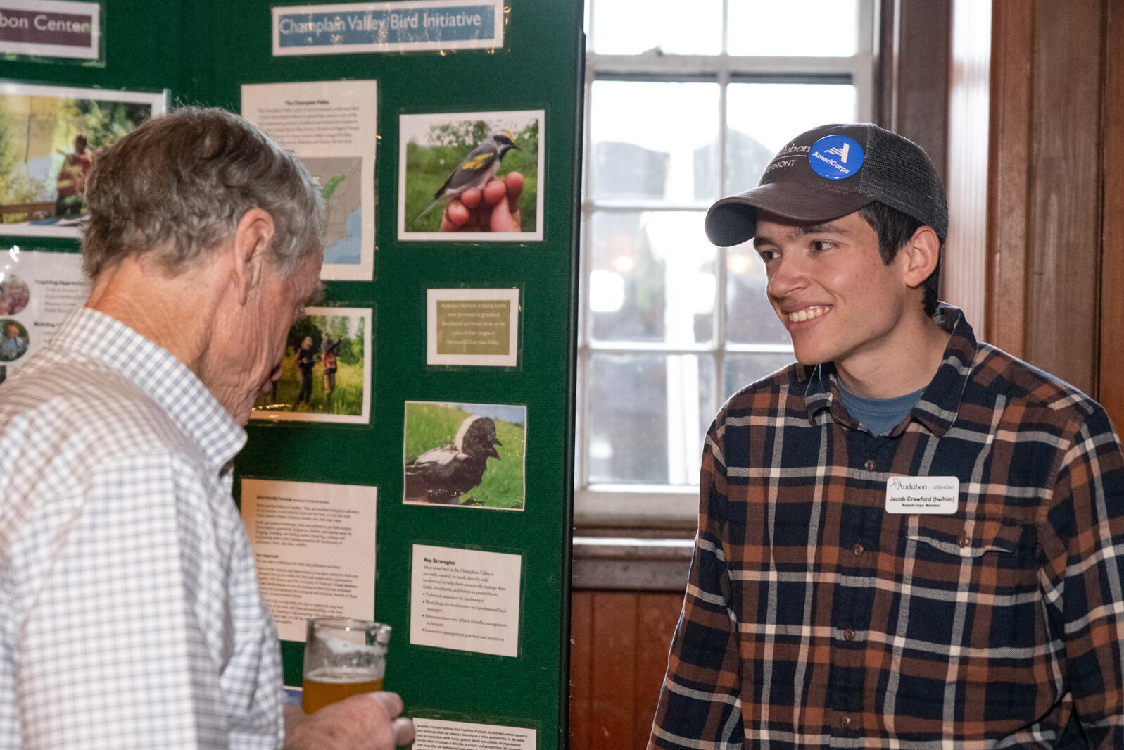 Jacob Crawford, right, smiles at an event attendee, left, who is reading from Audubon Vermont’s programming display. 
