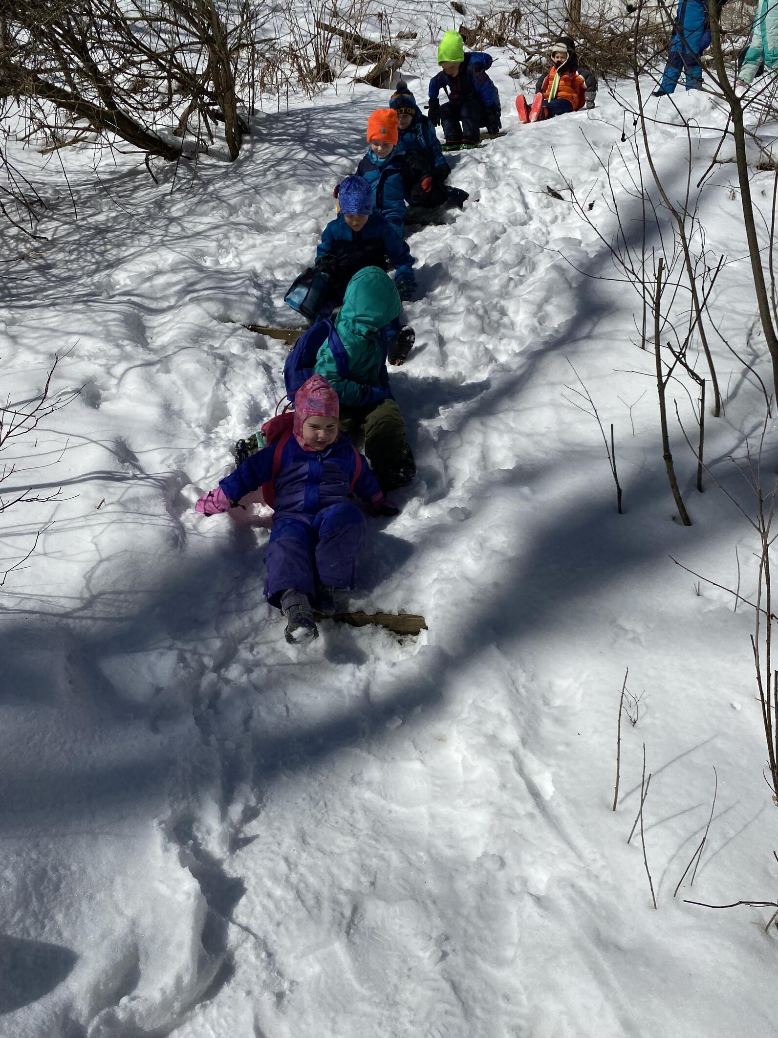 children slid down a snowy hill in a line