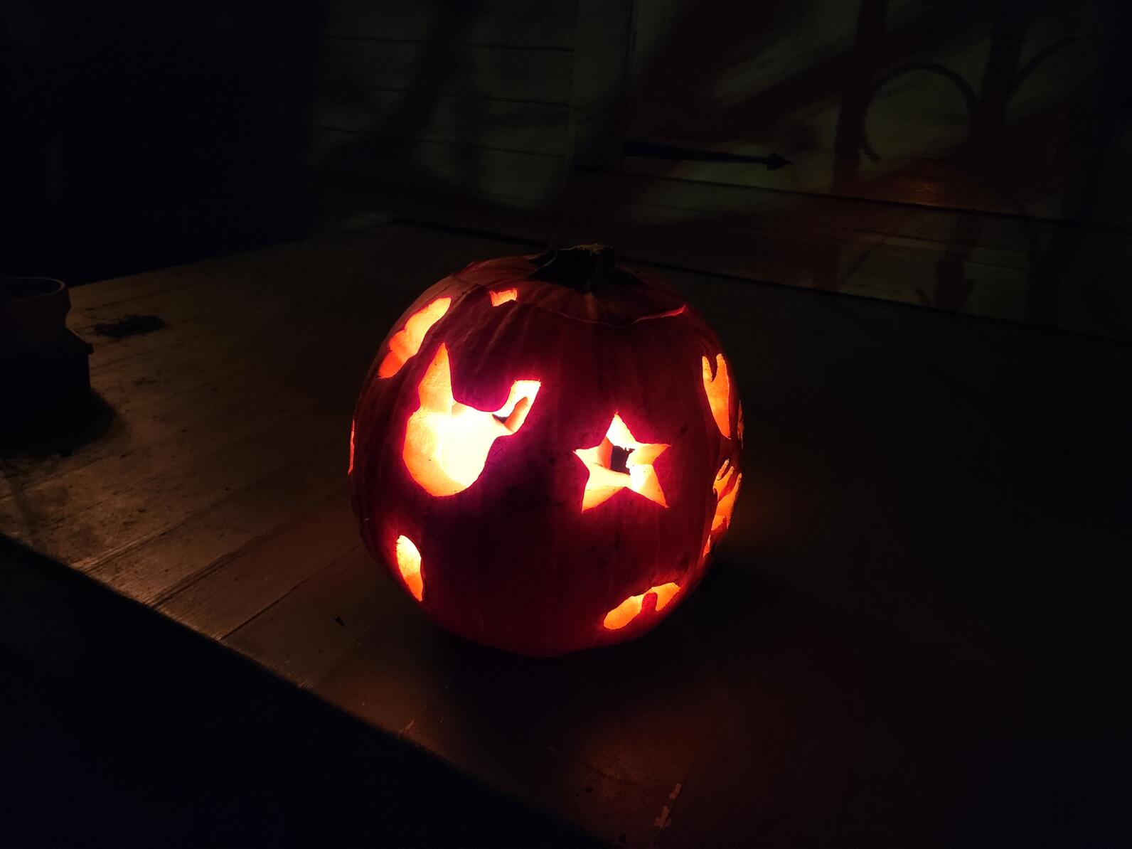 Jack o lantern in the dark with light shining out shapes cut into it.