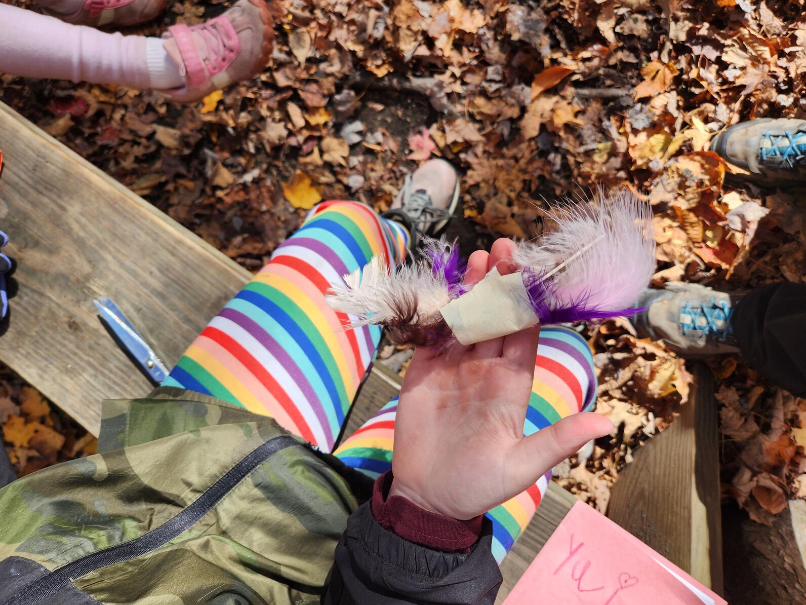 Child's hand holding out colorful feathers held together with masking tape