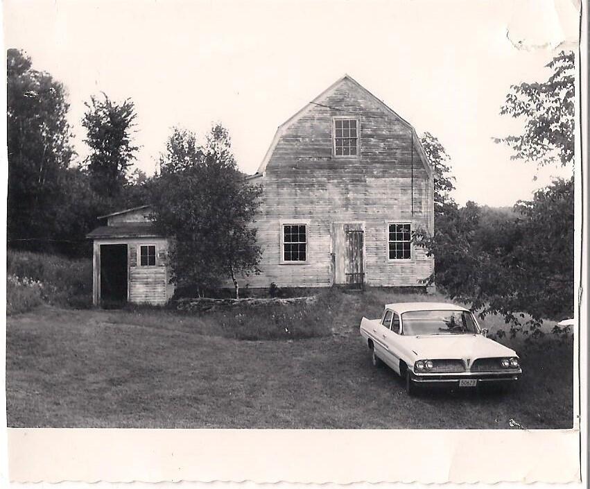 A black and white photo of the Education Barn with an antique car parked out front.