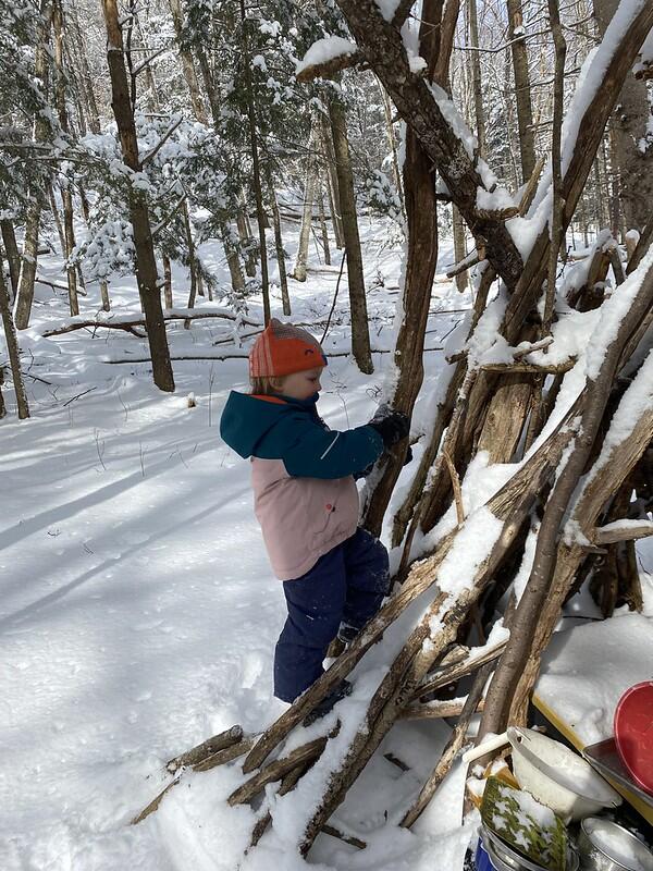 a child stands next to a stick fort