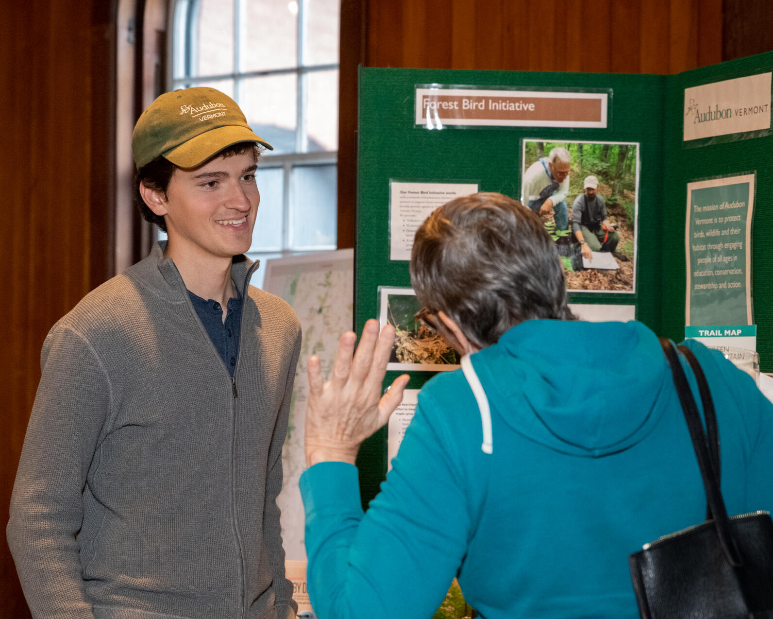 Thomas Patti, left, smiles at an event attendee, right, in front of Audubon Vermont’s programming display.