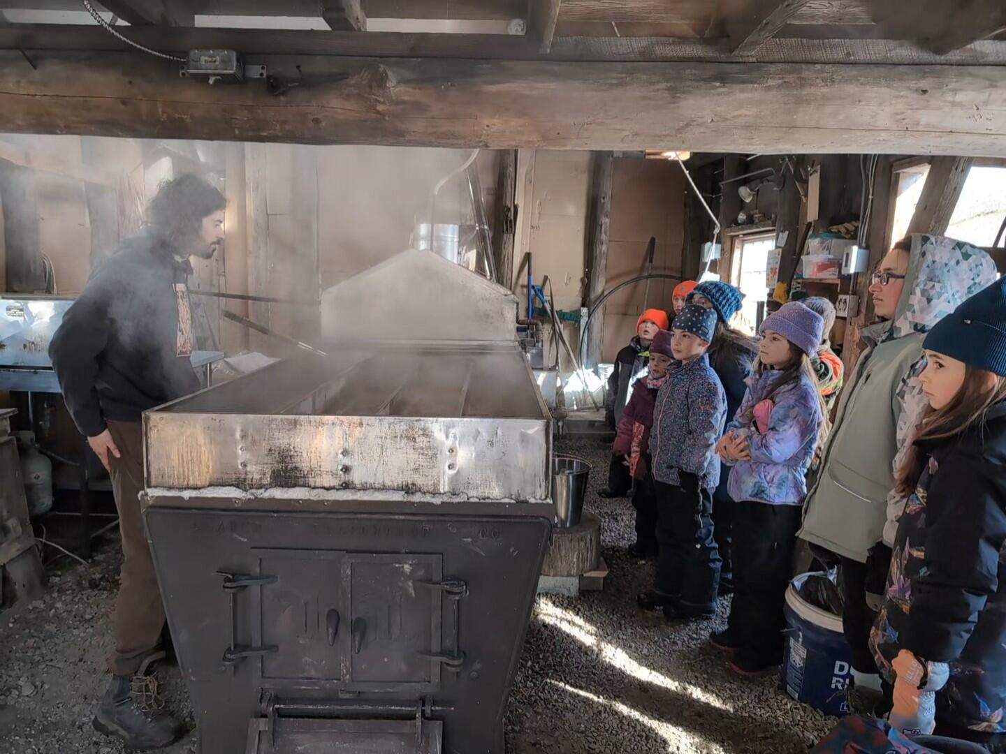 Inside the sugarhouse the sugarmaker stands on one side of the arch and evaporator with about a dozen students on the other side Inside the sugarhouse the sugarmaker stands on one side of the arch and evaporator with about a dozen students on the other side