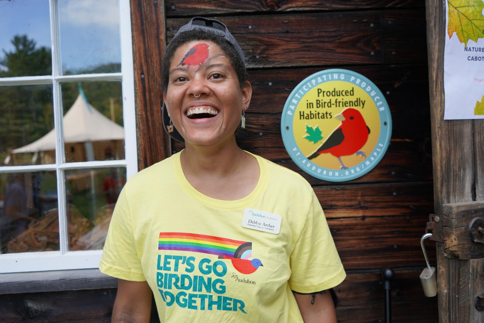Debbie smiles with a scarlet tanager painted on her face