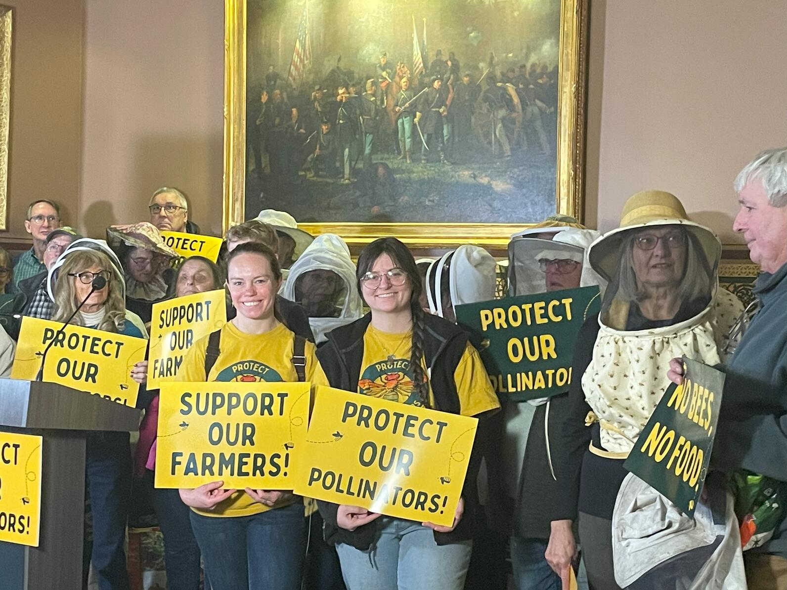 Women holding protect our pollinators and farms signs