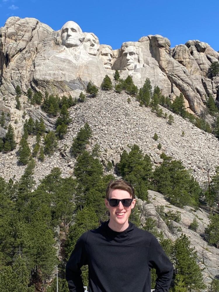 A photo of Spencer Ogden posing for a photo at the base of Mount Rushmore